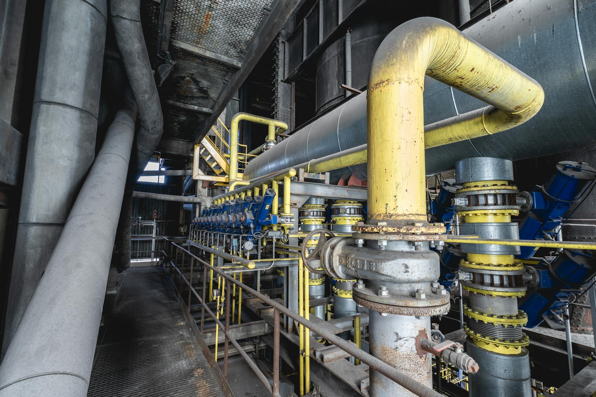 pexels-sonny-vermeer-505472791-17728787 Industrial pipeline system with yellow pipes, valves, and mechanical equipment inside a processing plant.